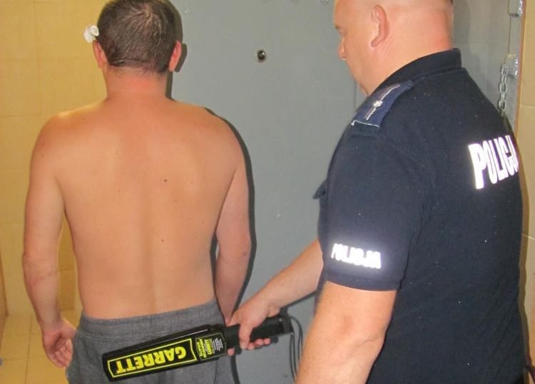 Policjant sprawdzający plecy mężczyzny wykrywaczem metalu Garrett.