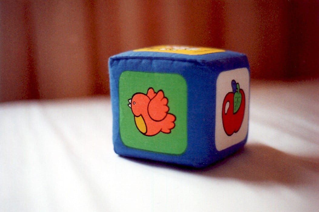 Miękka materiałowa zabawka w kształcie kostki z obrazkami ptaka i jabłka.