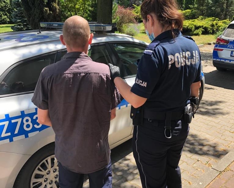 Policjant aresztujący mężczyznę obok radiowozu. Na mundurze policjanta widoczny jest napis POLICJA.