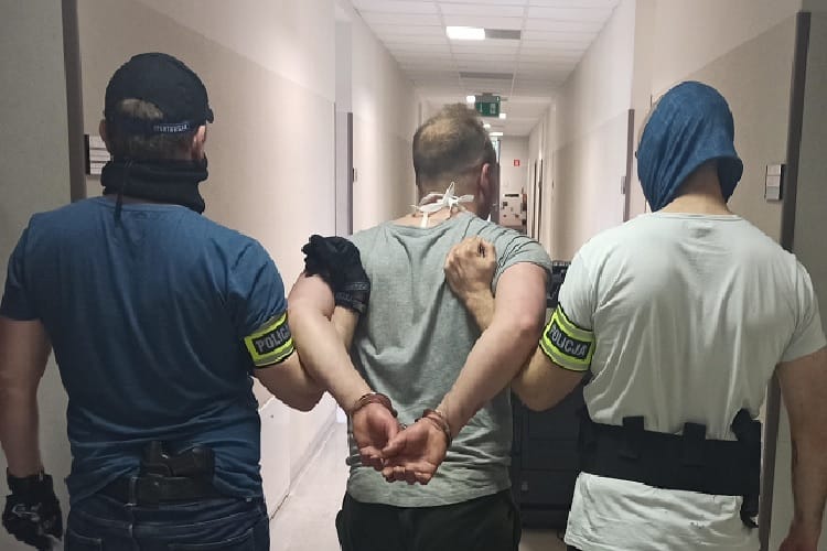 Policjanci eskortują skutego podejrzanego korytarzem szpitalnym.