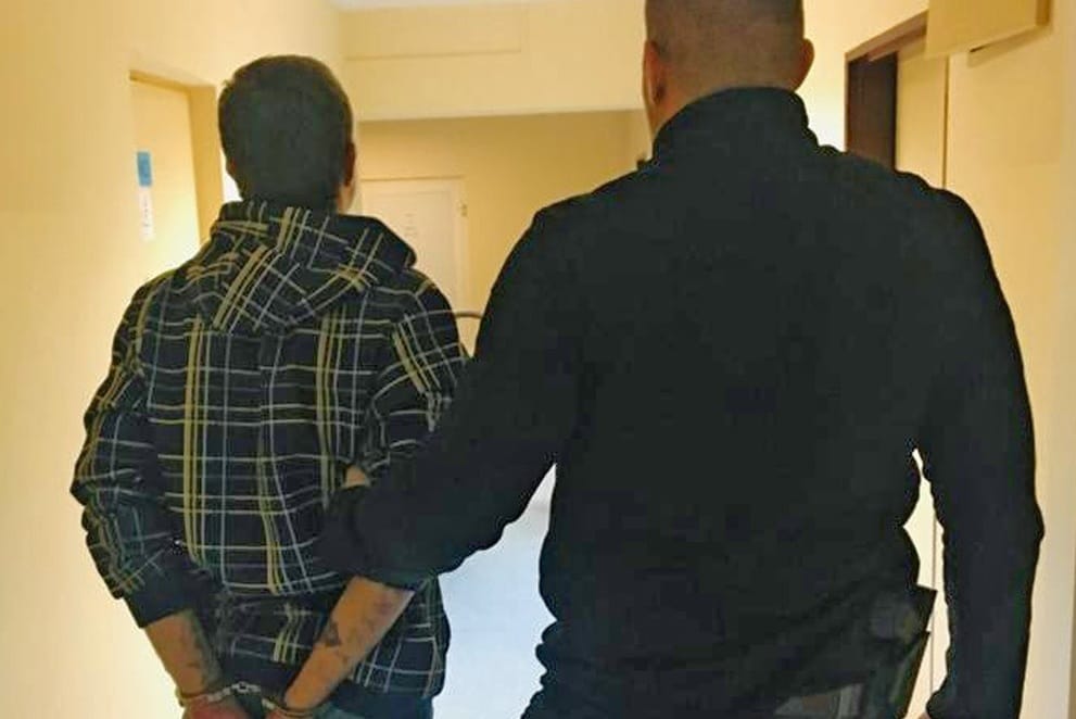 Policjant aresztujący podejrzanego w kajdankach na korytarzu.