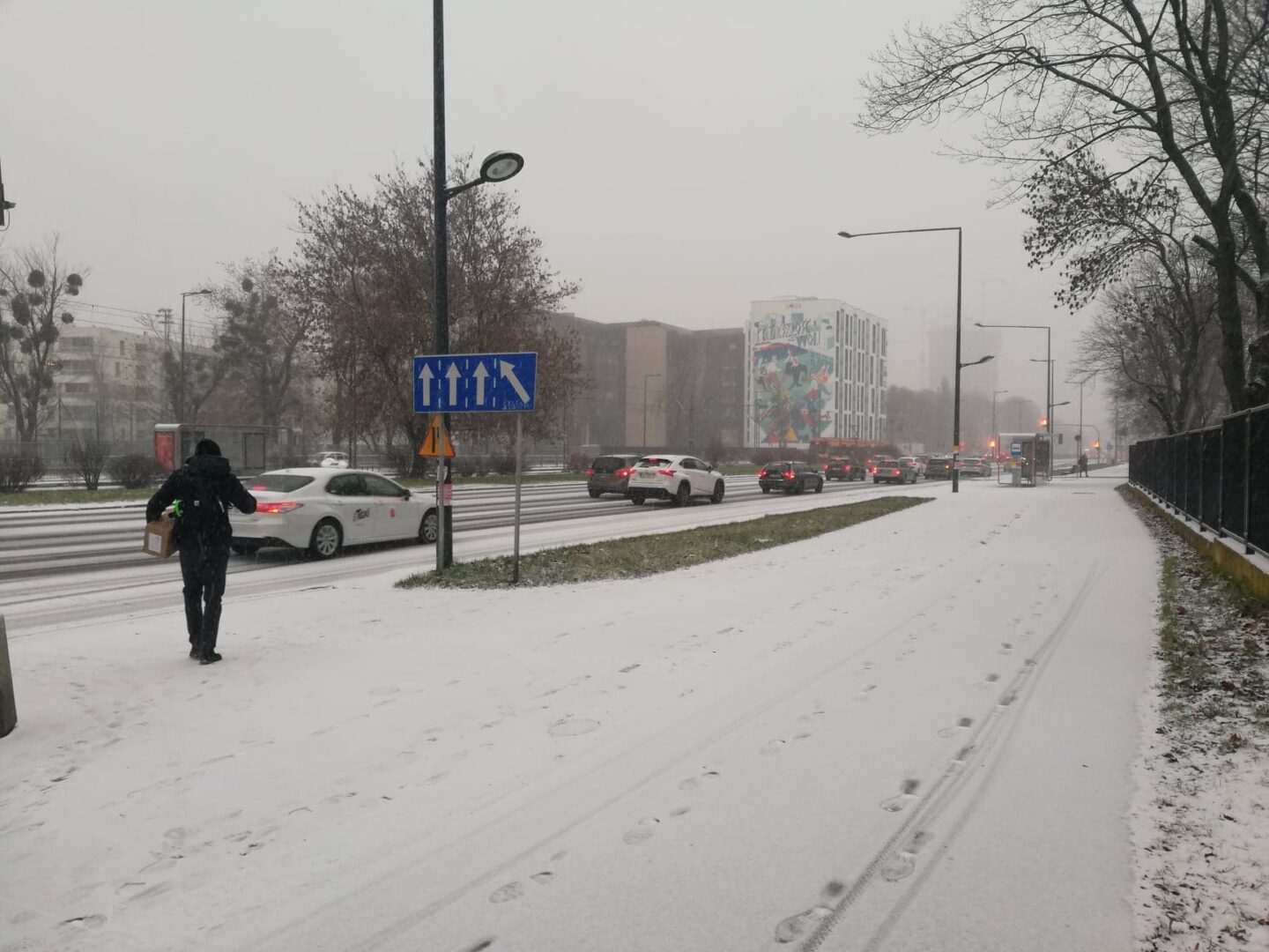 Scena z zaśnieżoną ulicą miasta, pieszymi i samochodami.
