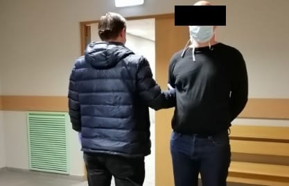 Policjant eskortujący podejrzanego w kajdankach.