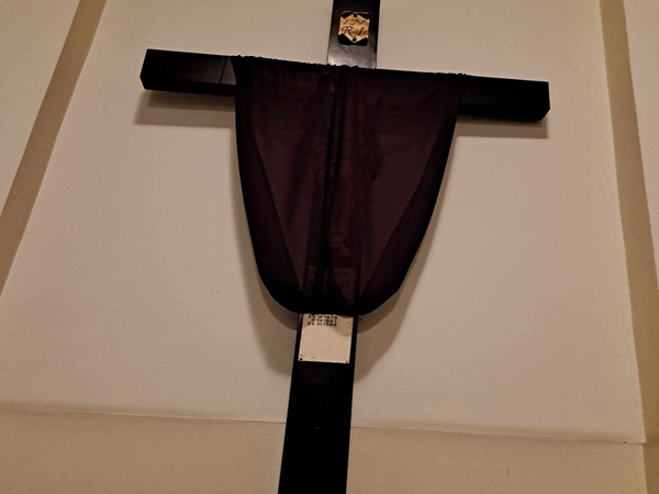 Ciemnofioletowa tkanina narzucona na prosty drewniany krzyż.