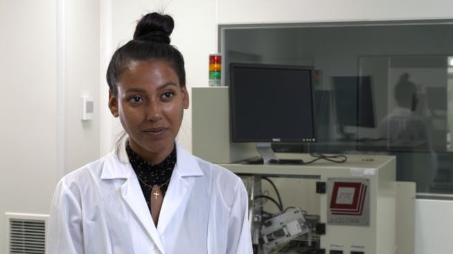 Młoda kobieta naukowiec w fartuchu laboratoryjnym patrzy w kamerę