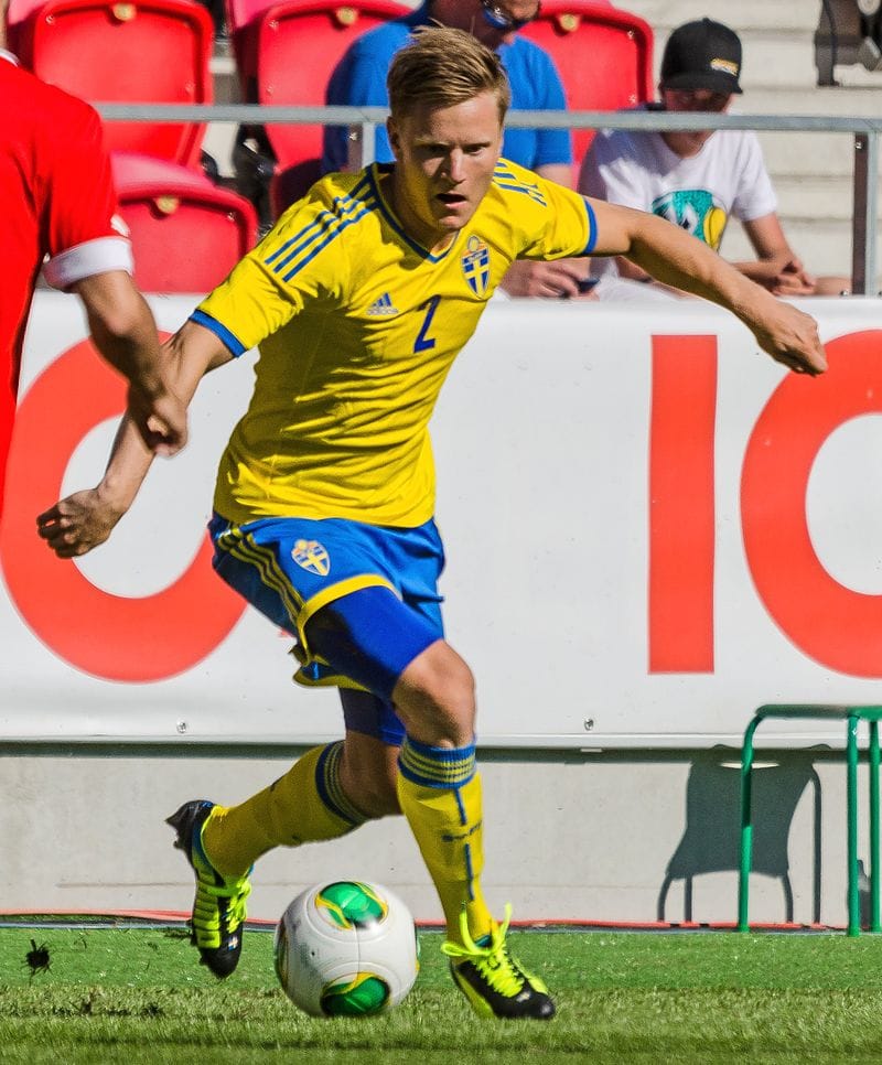 Szwedzki piłkarz, nr 2, drybluje piłkę podczas meczu.