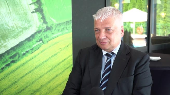 Biznesmen w garniturze podczas wywiadu, siedzący przed zielonym abstrakcyjnym obrazem.