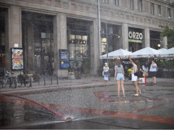 Ludzie cieszą się strumieniem wody przed restauracją Orzo w Warszawie.