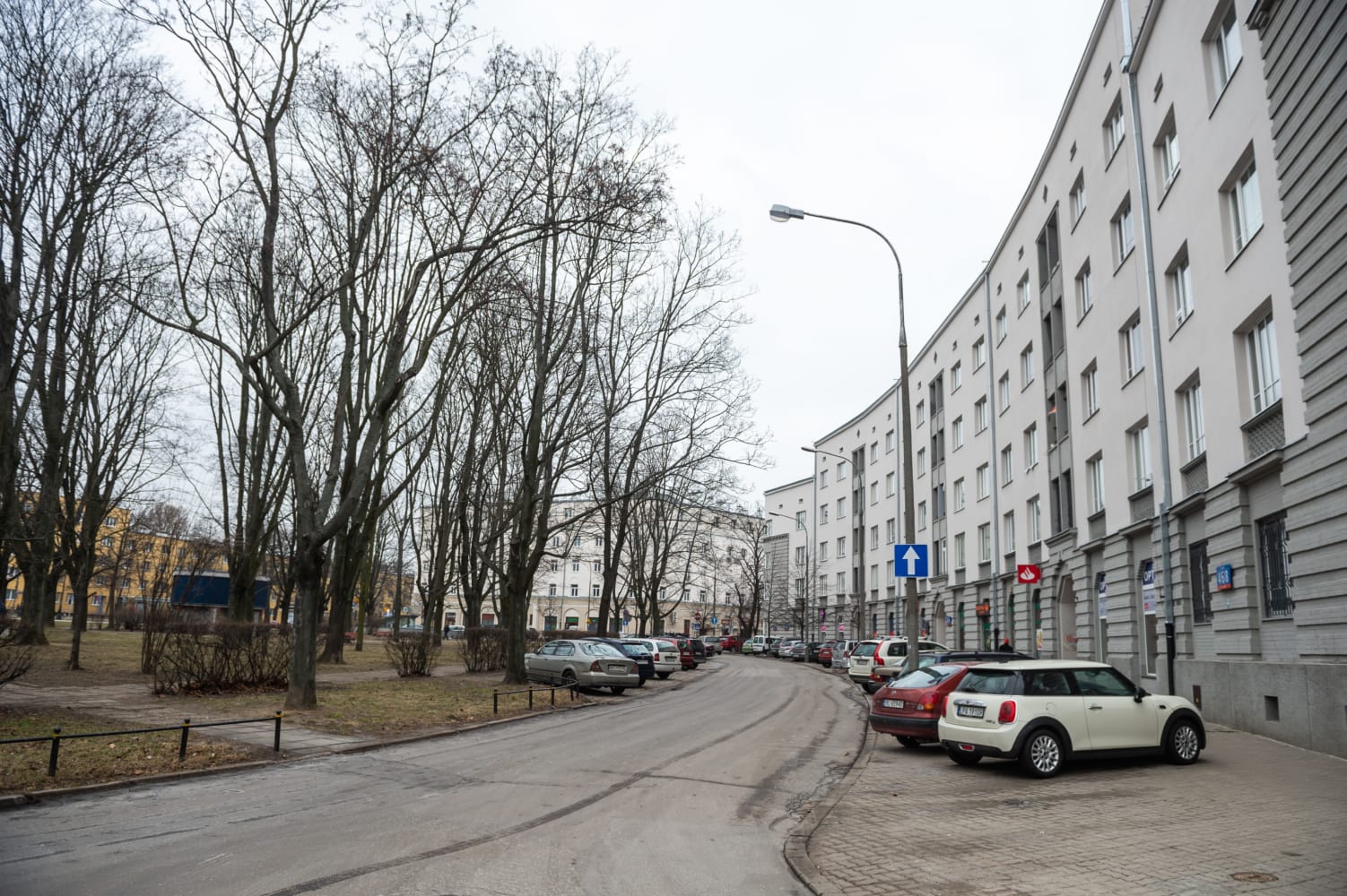 Samochody zaparkowane na ulicy osiedlowej, wzdłuż której stoją budynki mieszkalne, w pochmurny dzień.