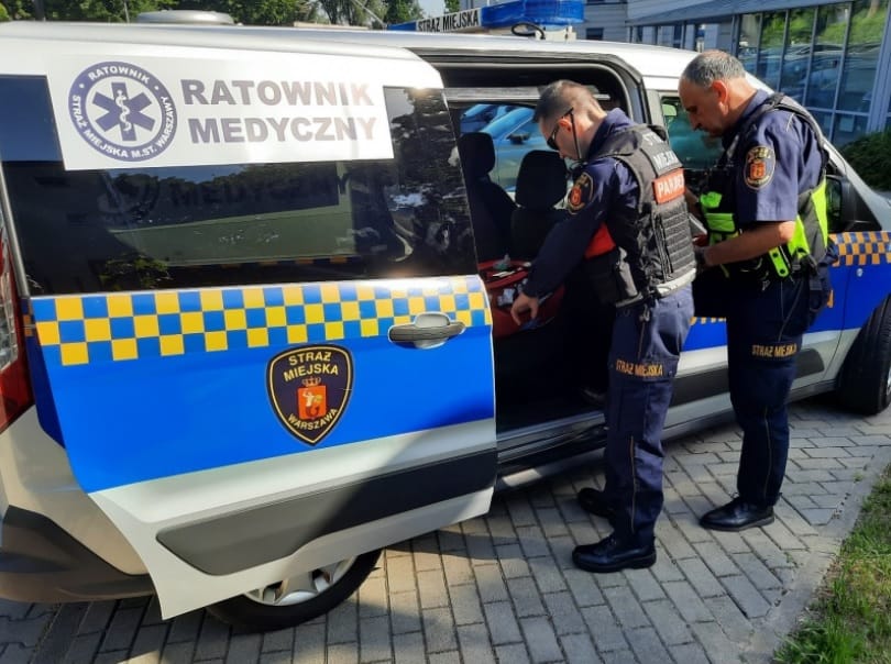 Warszawscy ratownicy medyczni ładują sprzęt medyczny do pojazdu pogotowia ratunkowego.