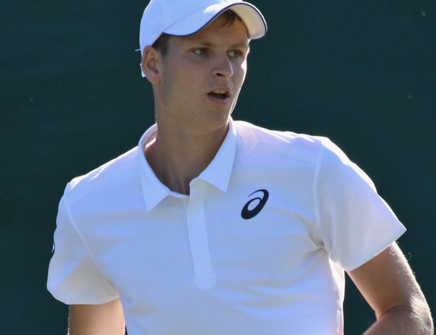 Tenisista ubrany w białą koszulkę i czapkę Asics