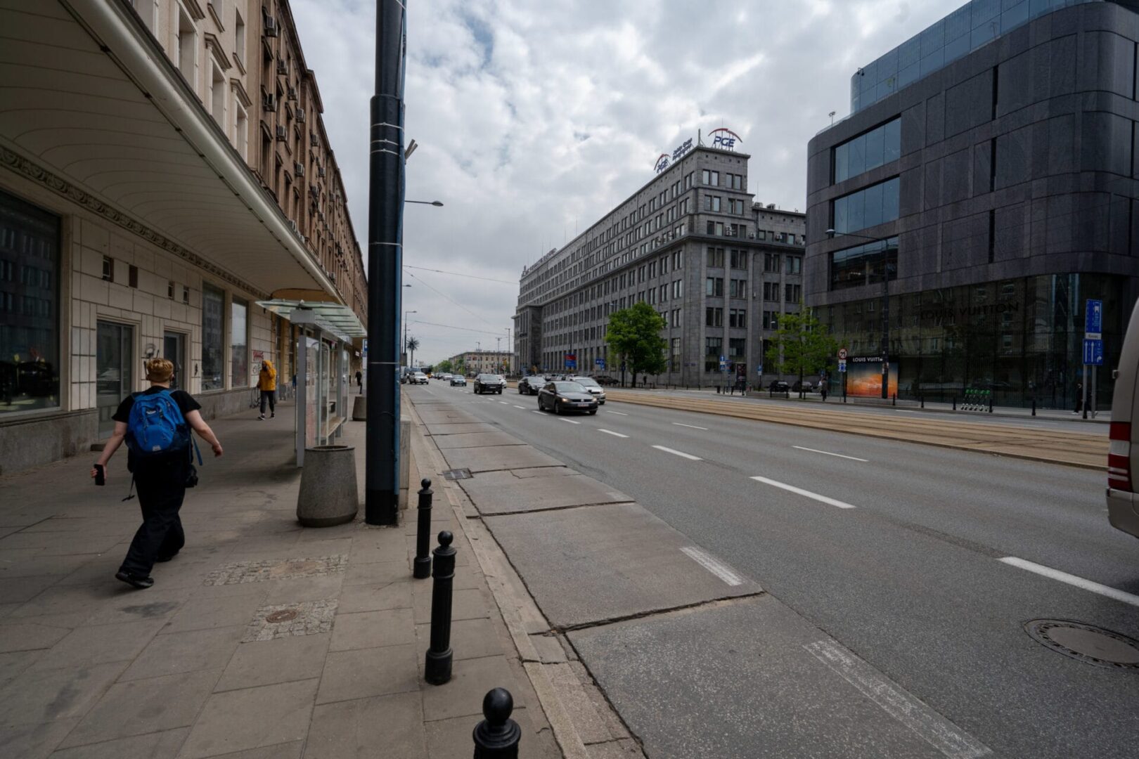 Widok na ulice Warszawy z nowoczesną i zabytkową architekturą, samochodami i pieszymi.