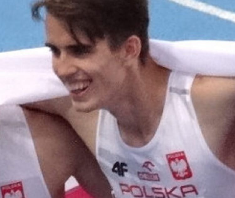 Uśmiechnięty polski sportowiec ubrany w biały podkoszulek z napisem „Polska” i polskim orłem.