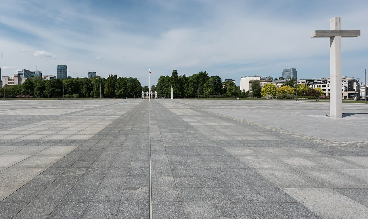 Pusty warszawski Plac Piłsudskiego z dużym krzyżem i panoramą miasta w tle.