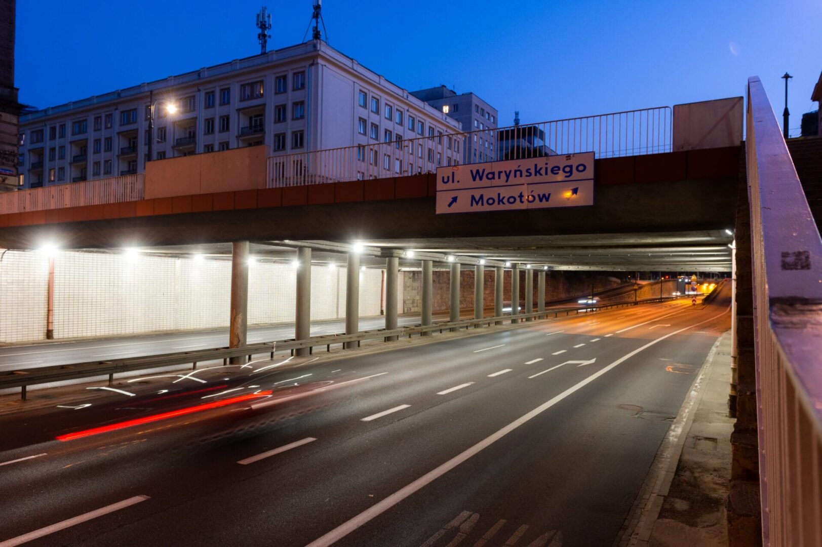 Nocny widok na przejście podziemne pod Warszawą, z tabliczkami wskazującymi na ulice Waryńskiego i Mokotów.
