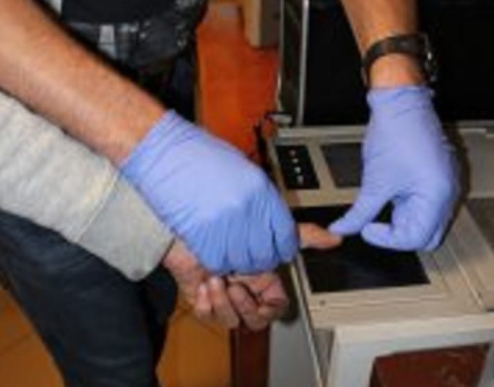 Zbliżenie dwóch dłoni w rękawiczkach korzystających ze skanera linii papilarnych.