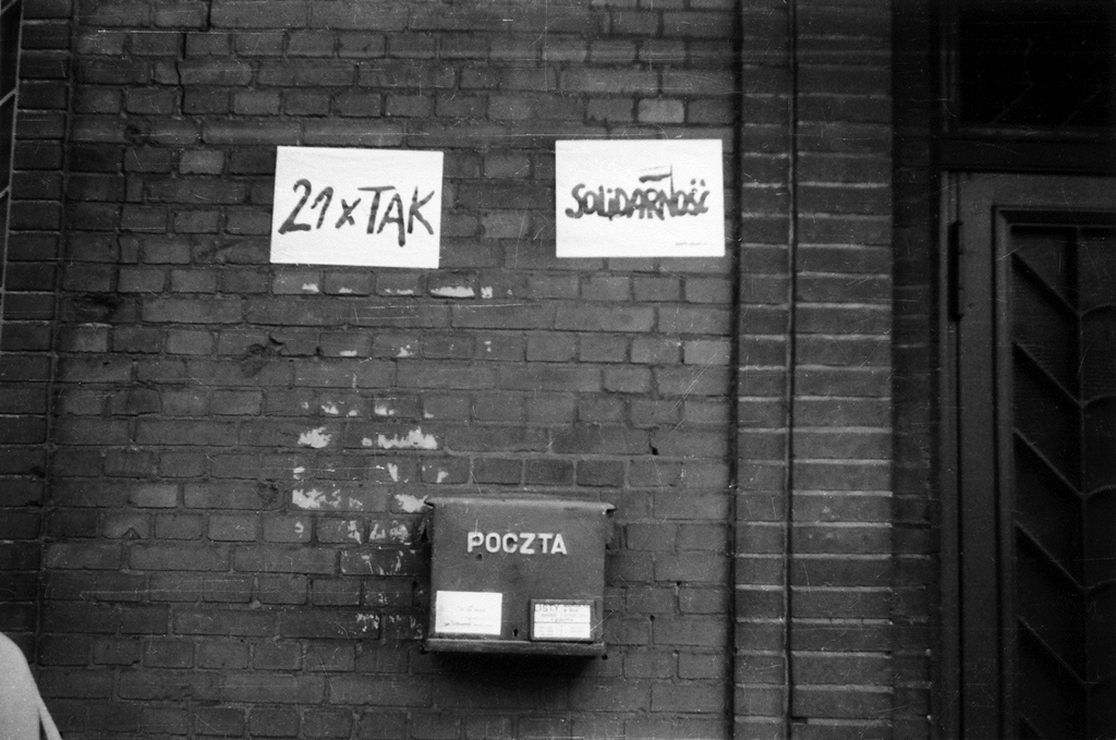 Ściana z cegły z napisem Solidarność i znakami 21xTAK oraz skrzynka pocztowa.