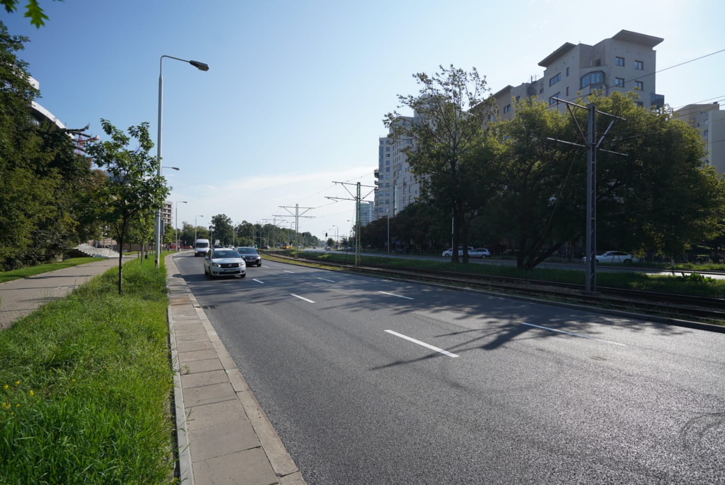 Samochody jadące ulicą miasta, wzdłuż torów tramwajowych i nowoczesnych budynków.