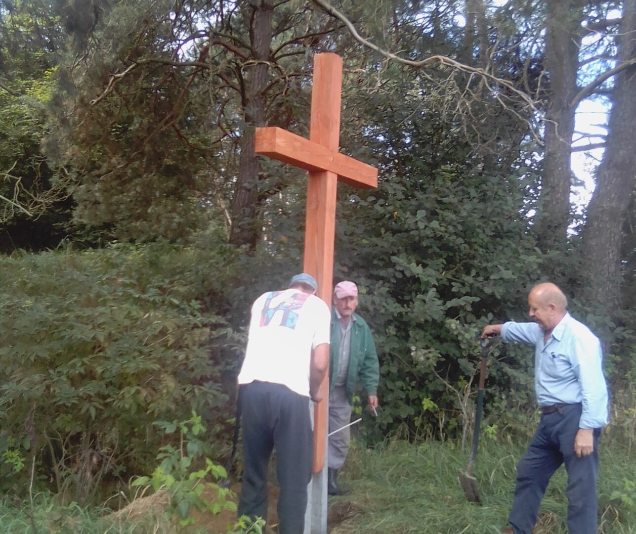 Trzech mężczyzn stawia duży drewniany krzyż na zewnątrz.