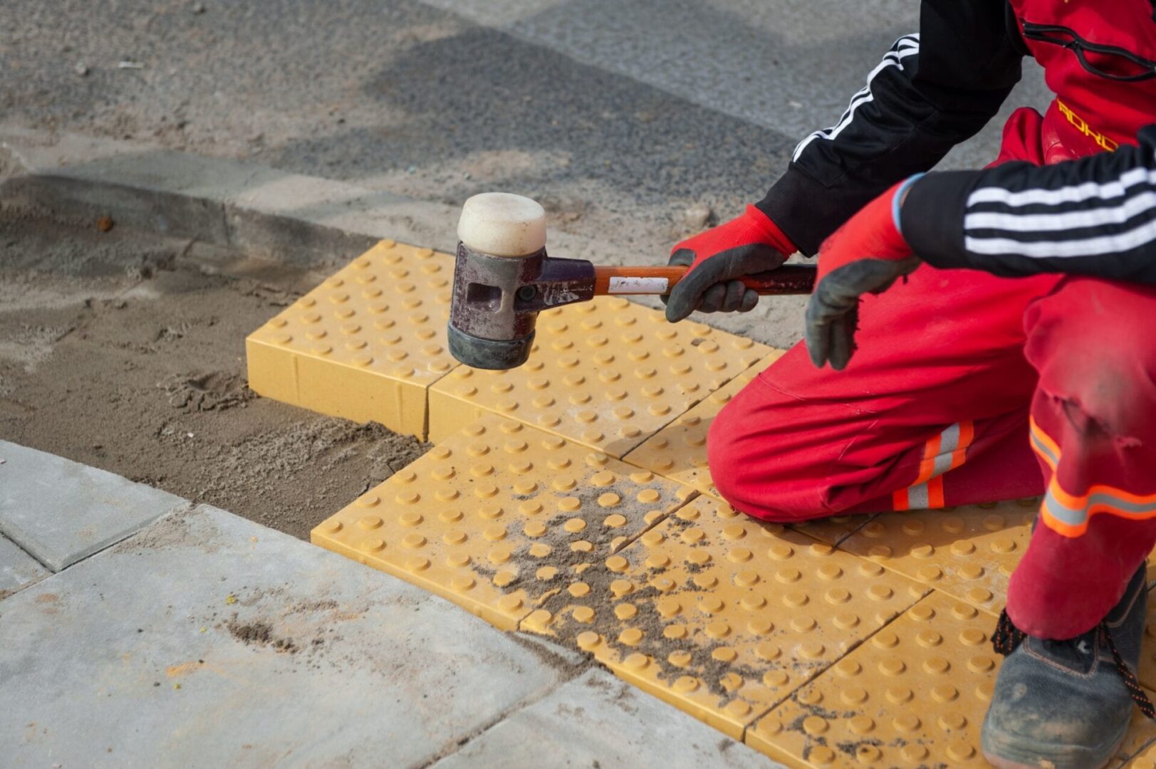Pracownik montujący nawierzchnię dotykową, używając gumowego młotka do układania żółtych, teksturowanych kostek brukowych.