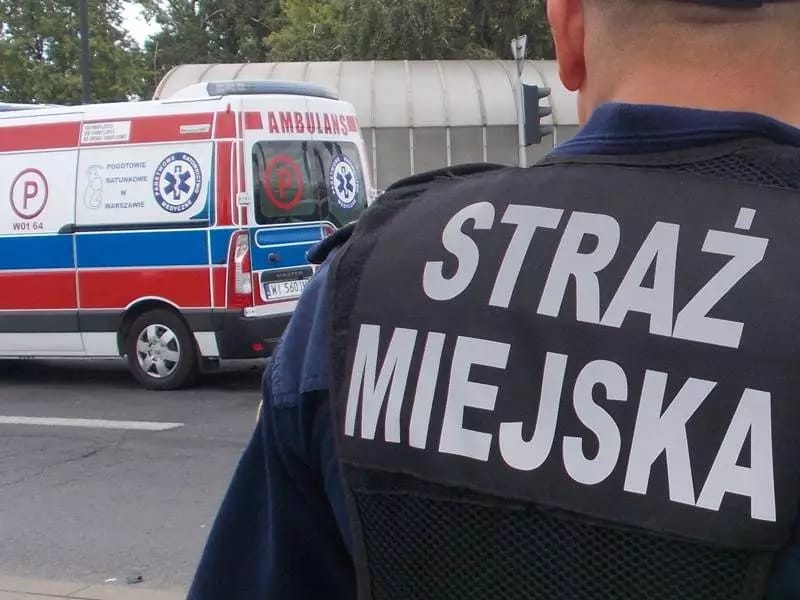 Funkcjonariusz Straży Miejskiej stoi w pobliżu ambulansu.