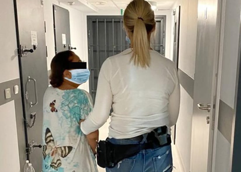 Policja eskortuje zamaskowaną kobietę korytarzem więziennym.