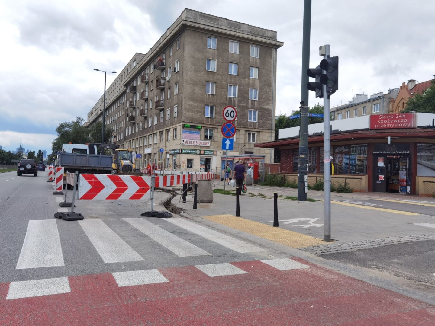 Budowa drogi w toku w pobliżu wielopiętrowego budynku. Widoczni są pracownicy i sprzęt.