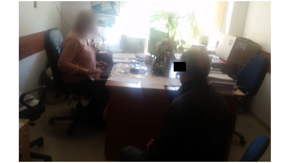 Dwie osoby przy biurku pracujące na komputerze. Twarz jednej osoby jest rozmazana dla prywatności.