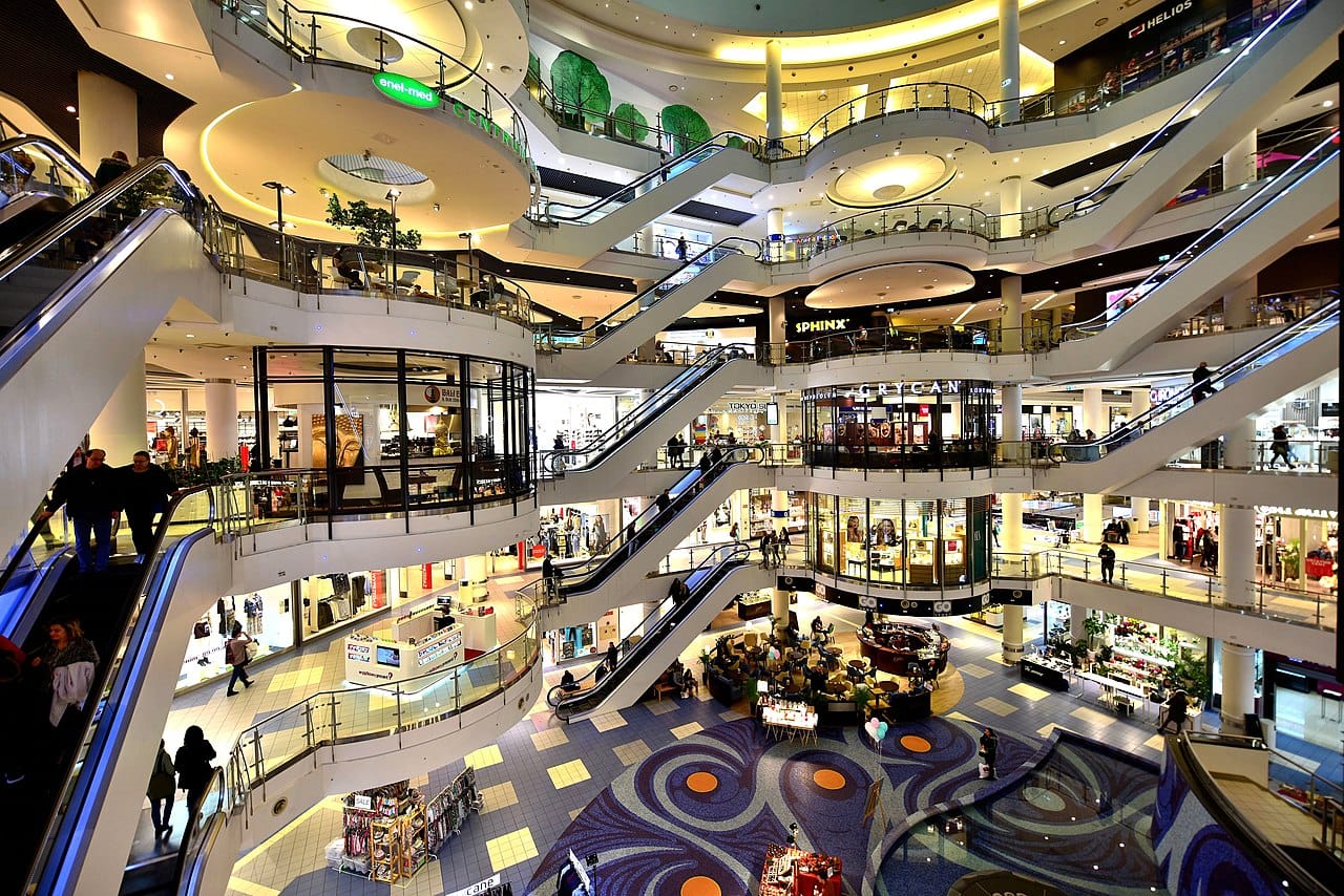 Wnętrze wielopiętrowego centrum handlowego z ruchomymi schodami i sklepami.