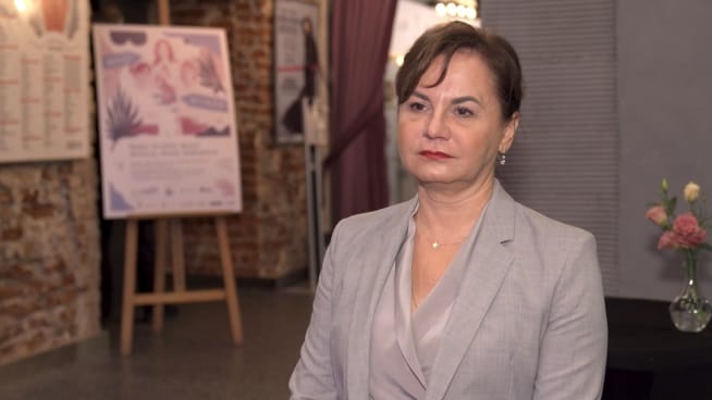 Portret kobiety w szarym blezerze, poważny wyraz twarzy.