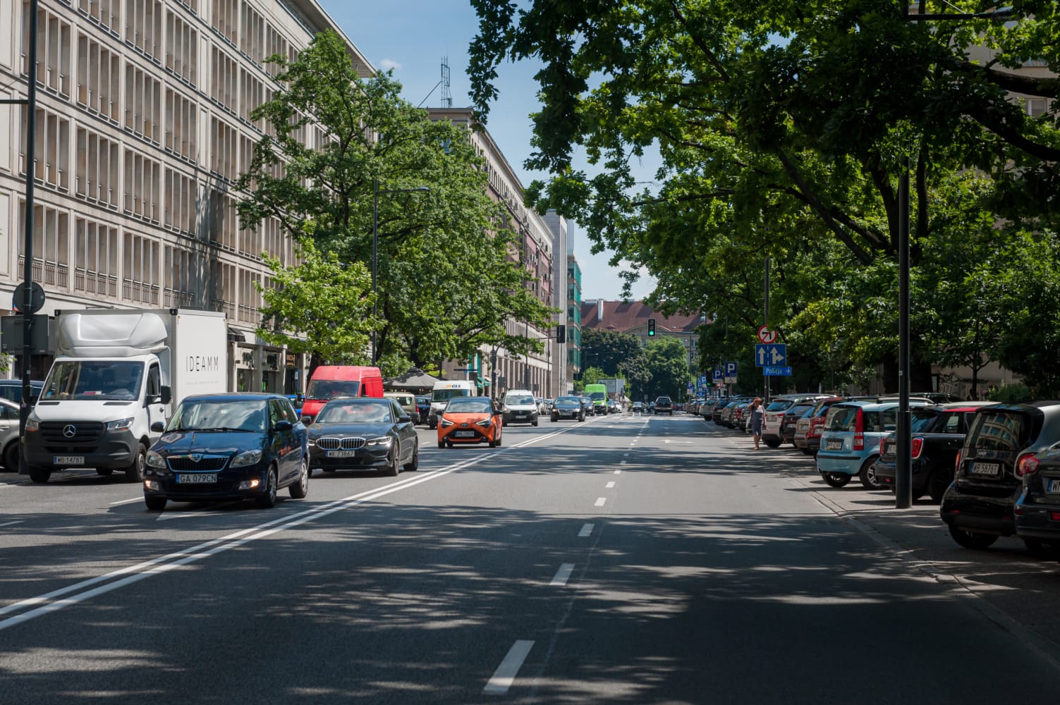 Samochody jadące ulicą miasta otoczoną drzewami i budynkami.