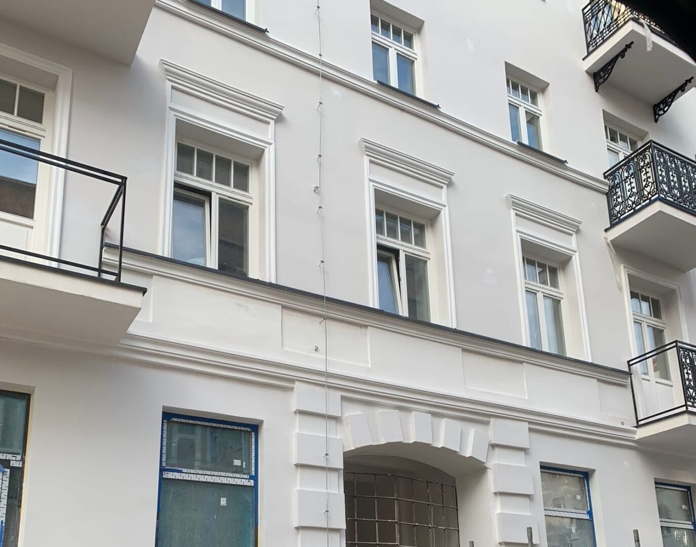 Odnowiona fasada budynku z ozdobnymi białymi ramami okiennymi i balkonami.
