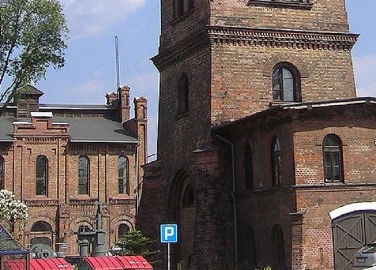 Historyczne budynki z cegły, prawdopodobnie dawna fabryka lub teren przemysłowy. Wyraźne detale architektoniczne i stare cegły.