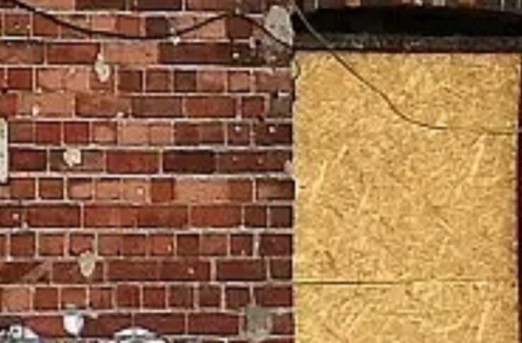 Uszkodzona ściana z cegieł z przykrywającą część sklejką