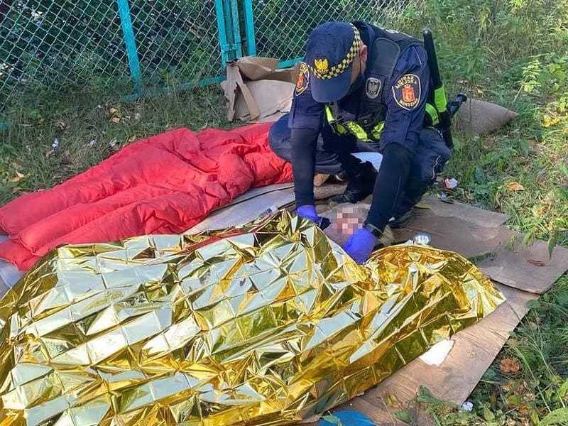 Policjant udzielający pomocy osobie owiniętej w koc termiczny.