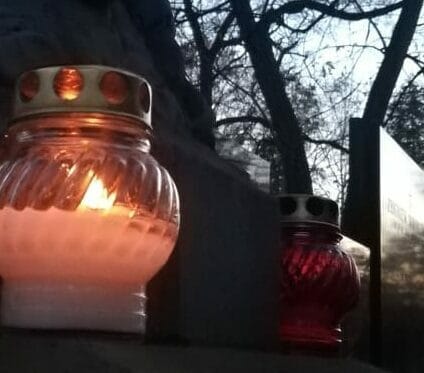 Dwie zapalone świece wotywne płoną w półmroku w pobliżu kamiennego pomnika.