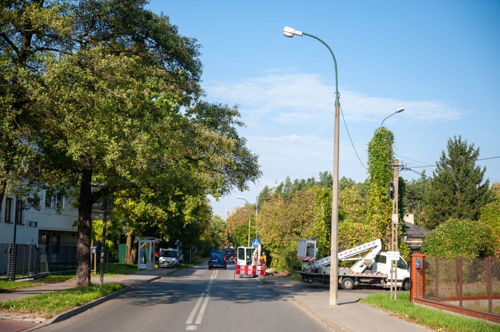 Scena uliczna z budową drogi, pracownikami i pojazdami użytkowymi.