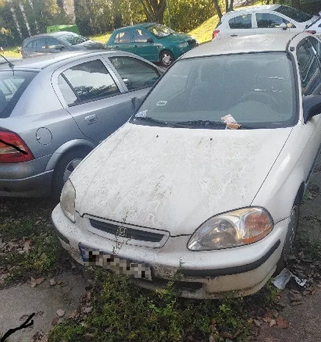 Brudny, biały samochód Honda Civic zaparkowany na parkingu z innymi samochodami