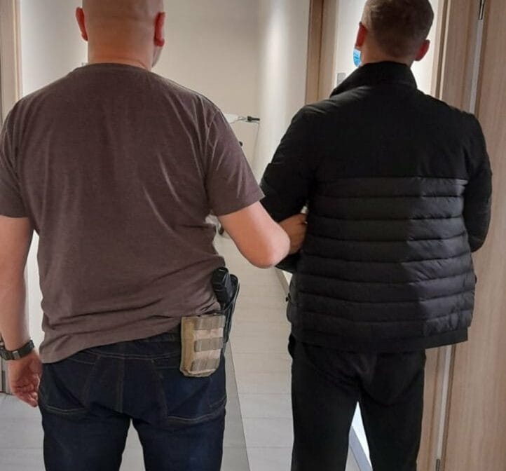 Policjant eskortujący podejrzanego korytarzem.