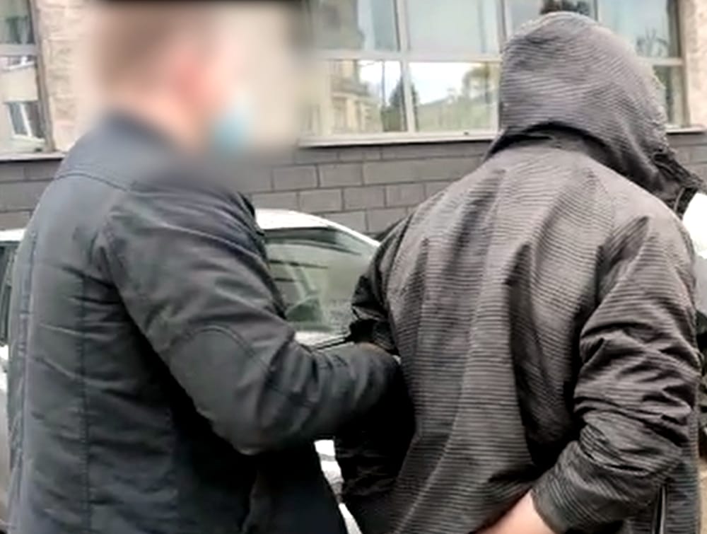 Policjant aresztujący podejrzanego w kajdankach w pobliżu samochodu.