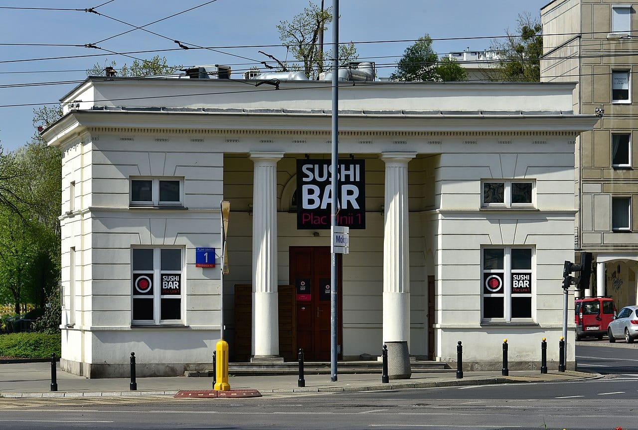 Biały budynek z kolumnami, szyldem „Sushi Bar” i widokiem na ulicę.
