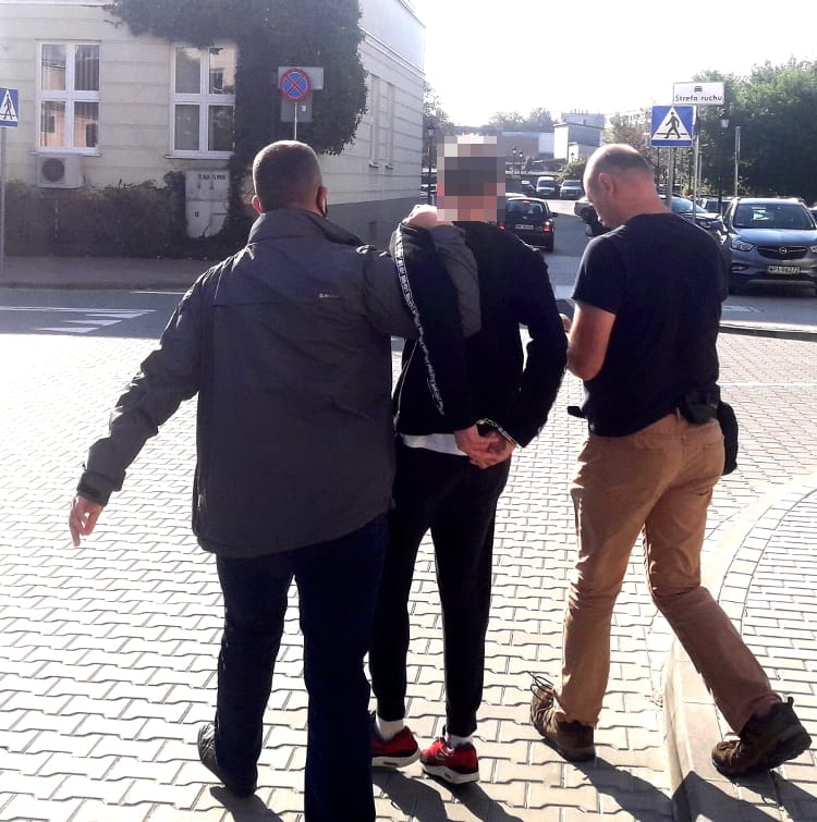 Dwóch policjantów eskortuje podejrzanego w kajdankach.