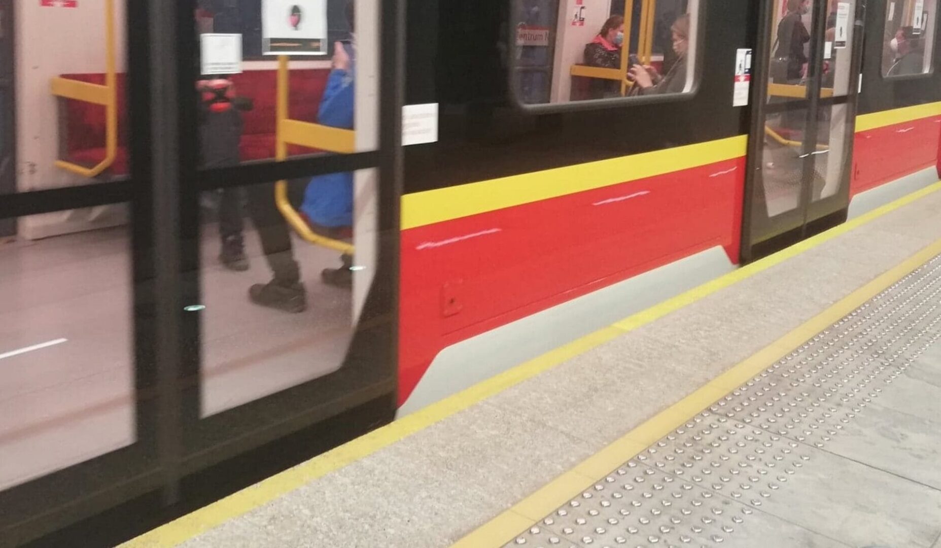 Drzwi pociągu metra w Warszawie otwierają się na peronie, pasażerowie wsiadają.