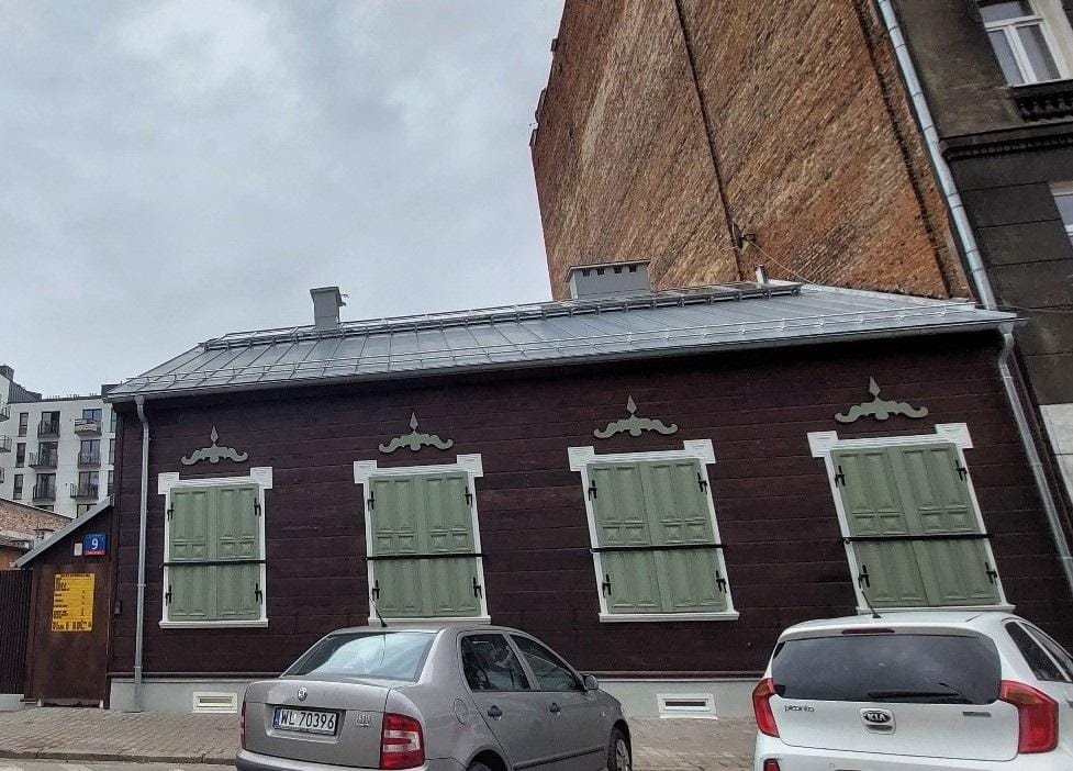 Ciemnobrązowy drewniany dom z zielonymi okiennicami i nowym metalowym dachem.