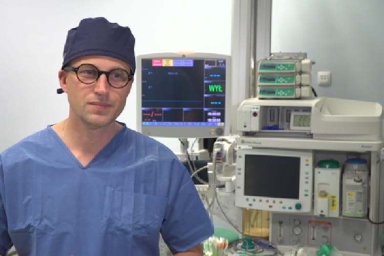 Chirurg w fartuchu na sali operacyjnej, widoczny sprzęt medyczny