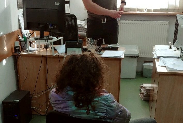 Kobieta z kręconymi włosami siedzi przy biurku w biurze, w pobliżu stoi mężczyzna.