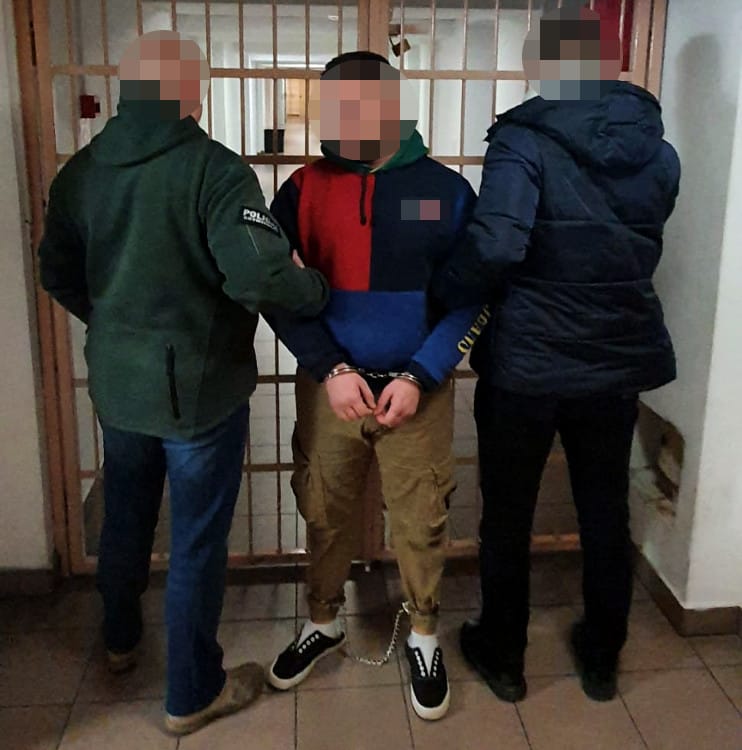 Skuty mężczyzna eskortowany przez dwóch funkcjonariuszy na korytarzu więziennym