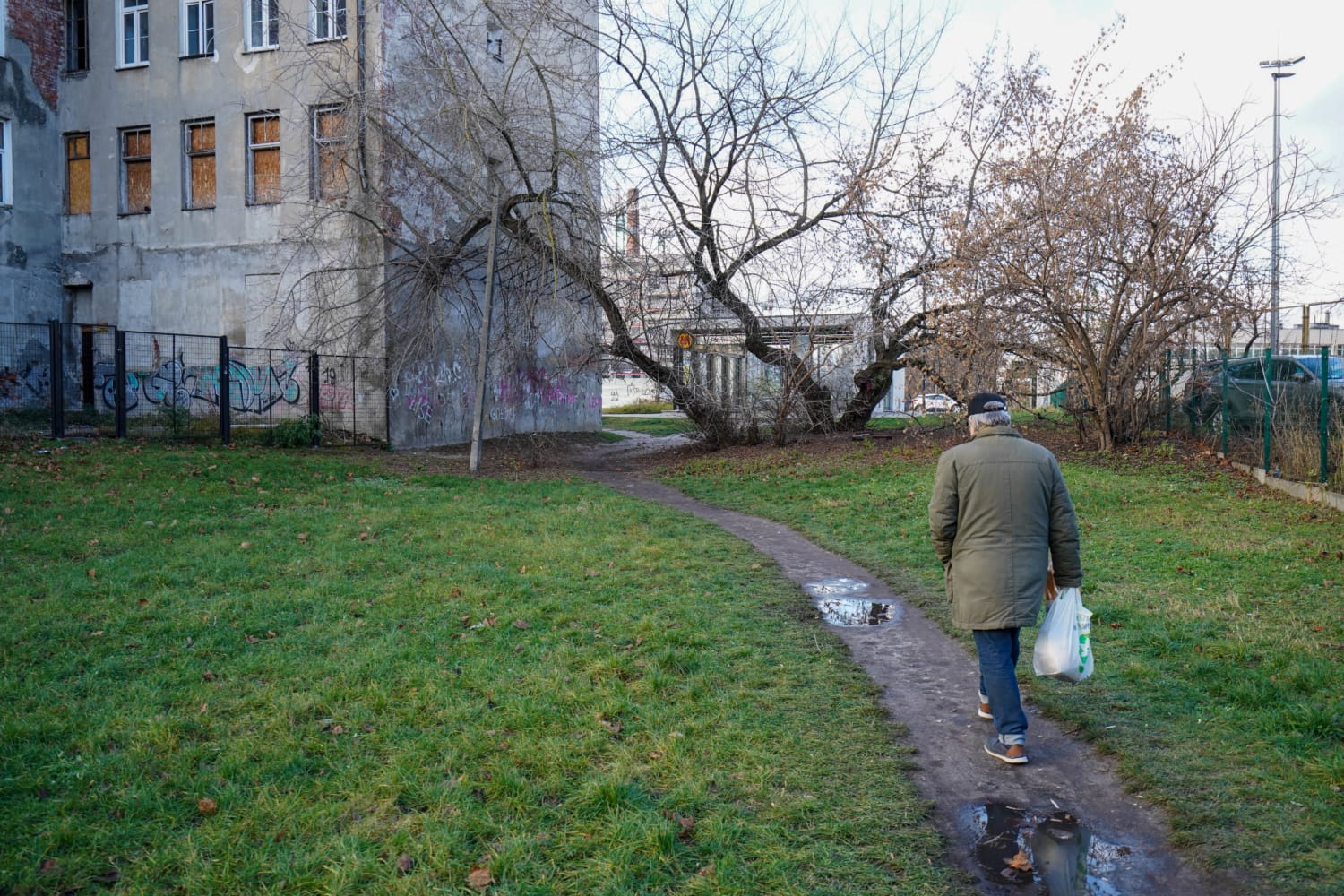 Starszy mężczyzna idzie ścieżką obok budynku pokrytego graffiti.