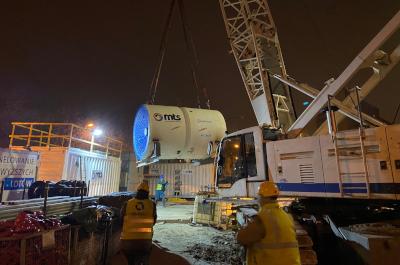 Dźwig podnosi duży element maszyny do drążenia tuneli (TBM) na placu budowy nocą.