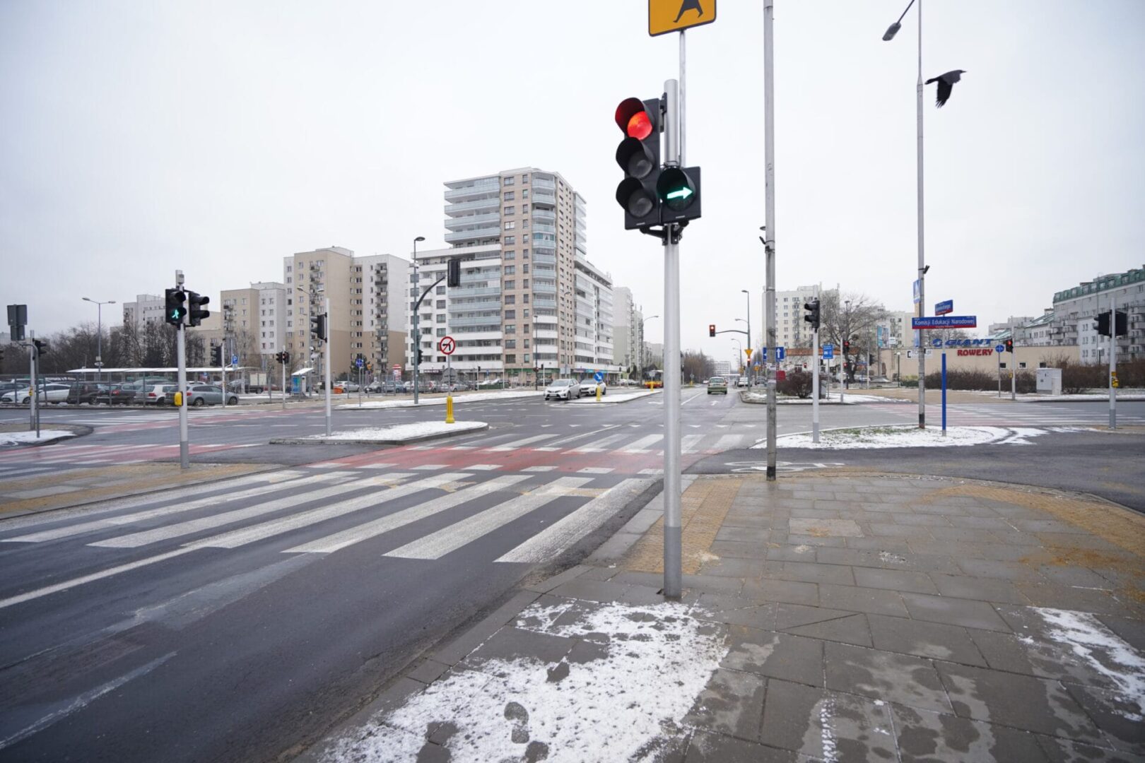 Opustoszałe skrzyżowanie z sygnalizacją świetlną, przejściem dla pieszych i śniegiem na ziemi.